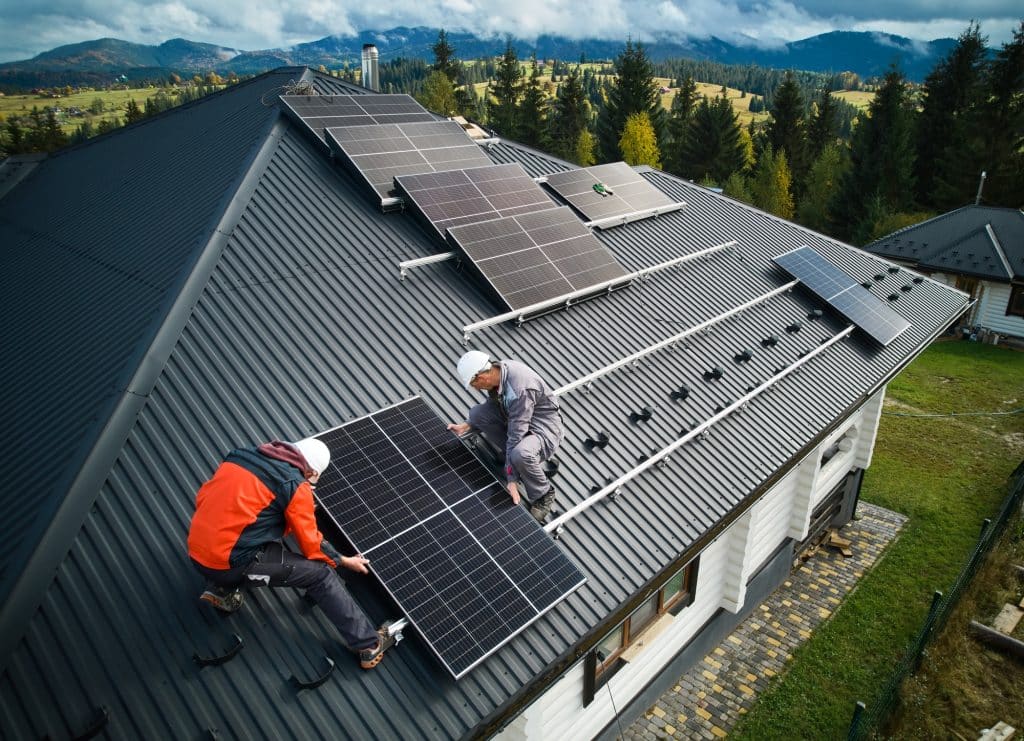 Men workers installing solar panels on roof of house.